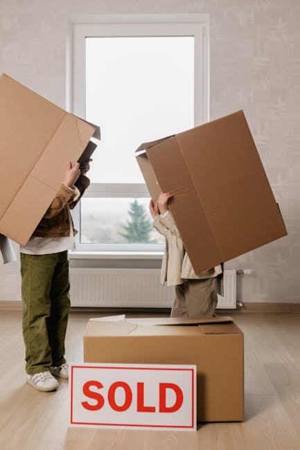A white commercial van is parked on a city street next to a multi-storey building. The rear doors of the van are open, revealing wrapped furniture, large cardboard boxes, and black rubbish bags, all o